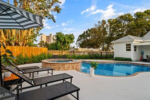 Beautiful backyard features a sparkling blue pool, comfortable lounge chairs under an umbrella, and lush tropical landscaping.
