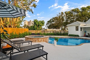 Beautiful backyard features a sparkling blue pool, comfortable lounge chairs under an umbrella, and lush tropical landscaping.
