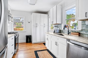 Bright and modern kitchen features sleek white cabinetry, stainless steel appliances, and hardwood flooring.
