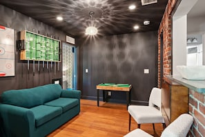 Unique living space offers a teal sofa, a pool table, exposed brick accents, and modern lighting, creating a stylish entertainment area.