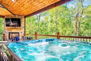 Luxury forest retreat features covered hot tub, crackling fireplace, and entertainment system surrounded by pristine wilderness views.