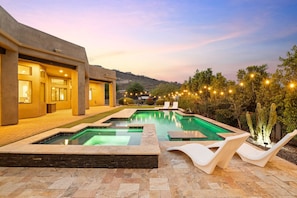 Pool with dinning table and hot tub with string lights near mountain views