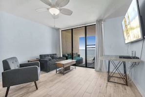 The living area has a love seat, accent chair, large TV, and balcony access.