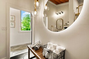 The bathroom features a round back-lit mirror and basic toiletries