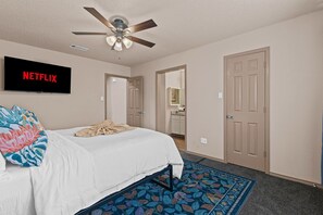 Serene bedroom with a white bed, teal headboard, and orange pillows, complemented by a green dresser and ceiling fan.