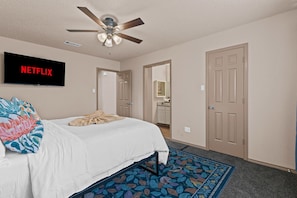 Serene bedroom with a white bed, teal headboard, and orange pillows, complemented by a green dresser and ceiling fan.