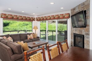 Cozy living area featuring a plush sectional sofa, stone fireplace with mounted TV, and expansive windows that open to a private patio.