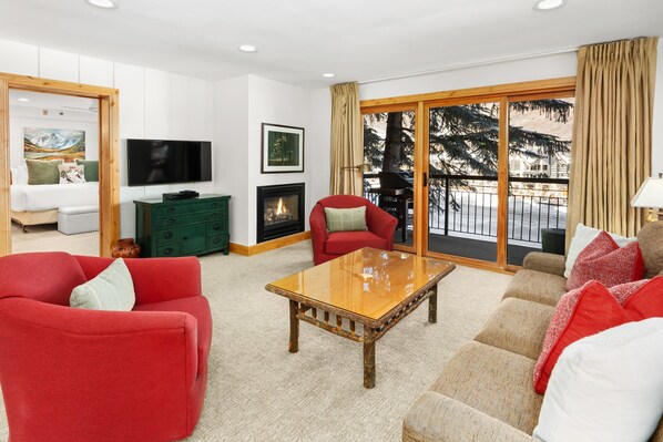 Cozy living area featuring a plush sectional sofa, fireplace with mounted TV, and expansive windows that open to a private patio.