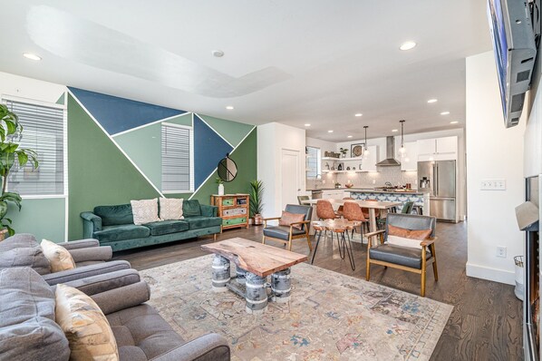 Welcoming living area with a vibrant green accent wall, large Smart TV, fireplace, and plush seating arranged to take in the serene outside views. (1st Floor)
