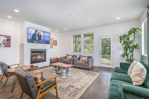 Welcoming living area with a vibrant green accent wall, large smart TV, fireplace, and plush seating arranged to take in the serene outside views. (1st Floor)