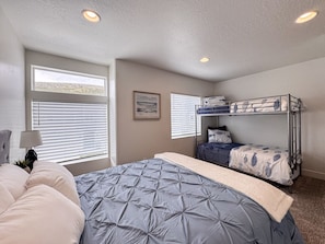 Spacious bedroom with queen bed, twin bunk beds, and bright natural light for cozy comfort.