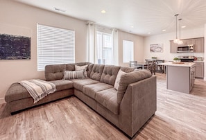 Spacious open-concept living area with cozy sectional, bright windows, and seamless kitchen connection.