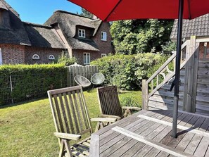 Terrasse hinter dem Haus mit Tisch, Stühlen und einem Garten mit Loungesesseln. 