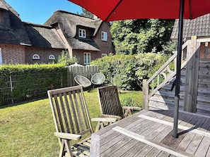 Terrasse hinter dem Haus mit Tisch, Stühlen und einem Garten mit Loungesesseln.