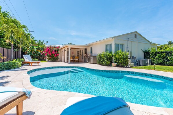 Relax in your own private West Palm Beach oasis—this fully fenced backyard features a sparkling pool, tropical landscaping, covered outdoor dining, BBQ grill, and sun loungers for the ultimate