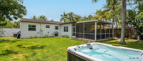 Spacious, fully fenced backyard retreat featuring a private hot tub, tropical landscaping, and a BBQ grill station—perfect for lounging, grilling, or unwinding under the palms