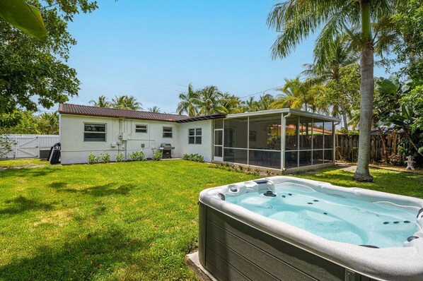 Spacious, fully fenced backyard retreat featuring a private hot tub, tropical landscaping, and a BBQ grill station—perfect for lounging, grilling, or unwinding under the palms
