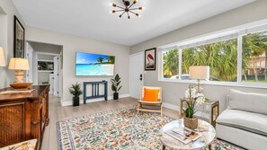 Step into a sunlit, artful living space with tropical flair—featuring bold pops of orange, vintage wood accents, and a large smart TV for cozy nights in. The perfect blend of El Cid charm and West Palm warmth