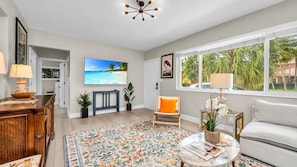 Step into a sunlit, artful living space with tropical flair—featuring bold pops of orange, vintage wood accents, and a large smart TV for cozy nights in. The perfect blend of El Cid charm and West Palm warmth