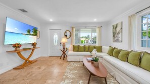 This bright and airy living room offers plenty of space for up to 6 guests to relax in comfort. Featuring a wraparound sectional with plush green accent pillows, a smart TV, and tasteful tropical decor, it's the perfect place to unwind after exploring WPB