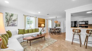 This bright and airy living room offers plenty of space for up to 6 guests to relax in comfort. Featuring a wraparound sectional with plush green accent pillows, a smart TV, and tasteful tropical decor, it's the perfect place to unwind after exploring WPB
