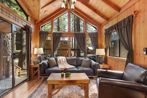 Cozy up in the cabin’s inviting living room—featuring a fireplace, TV, AC mini split, and large windows that frame the towering pines and let in the crisp mountain air. Step right out onto the patio for fresh forest views.
