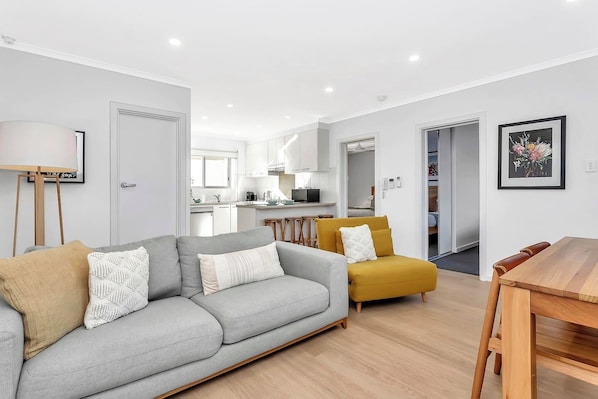 The compact open-plan living area features soft sofas, a soothing colour palette, and a TV, offering a cosy space to relax and feel at home.