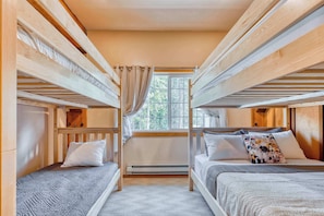 A cozy and inviting bedroom featuring two queen beds and two twin beds, perfect for families or small groups. The room is styled with rustic wood accents and plush bedding for maximum comfort.