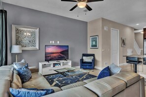 Open living space with large sofa, TV, and back patio access