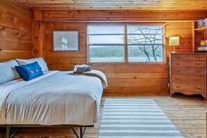 Charming, cozy king bedroom with rustic wood paneling and lake views. Perfect for a relaxing stay.