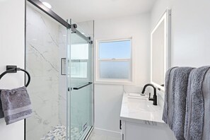 Modern bathroom with full shower - towels, hair dryer, hand soap, and essentials like shampoo, conditioner, and body wash all provided. 