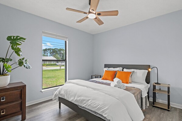 Unwind in this serene and sunlit bedroom featuring a comfy queen bed, crisp linens, and vibrant accents that add a cheerful touch. Enjoy peaceful views from the large window and rest easy with blackout shades, soft lighting, and thoughtful touches throughout.