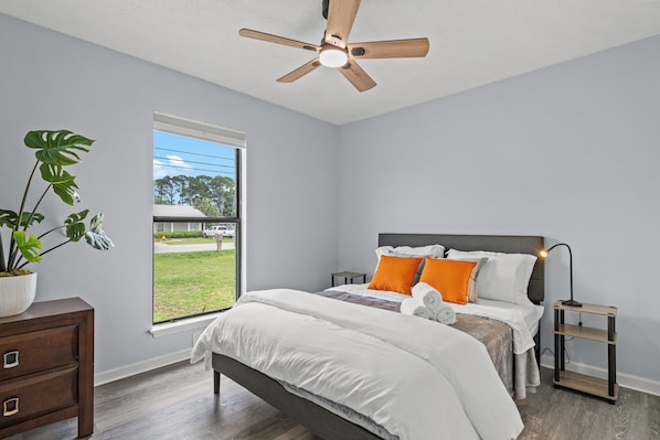 Unwind in this serene and sunlit bedroom featuring a comfy queen bed, crisp linens, and vibrant accents that add a cheerful touch. Enjoy peaceful views from the large window and rest easy with blackout shades, soft lighting, and thoughtful touches throughout.