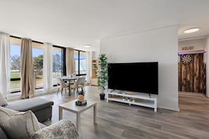 Open-plan layout with dining for four, smart TV, and oversized windows.