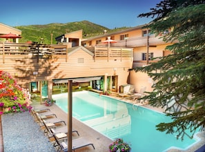 Dive into the refreshing shared pool surrounded by lush flowers and comfortable lounge chairs, perfect for soaking up the sun against a stunning mountain backdrop.