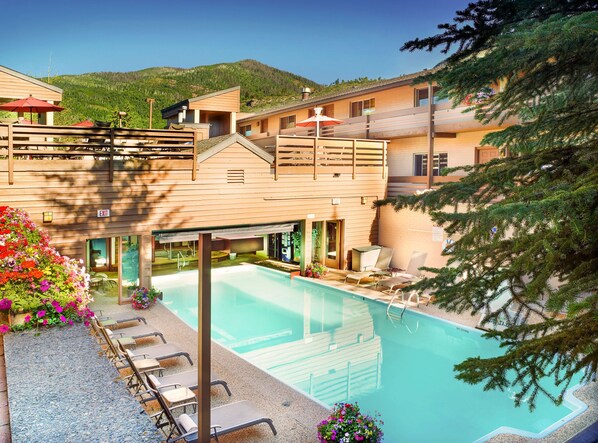 Enjoy the sunshine and vibrant flowerbeds surrounding the shared pool and hot tub area, perfect for relaxation in a cozy alpine condo setting.