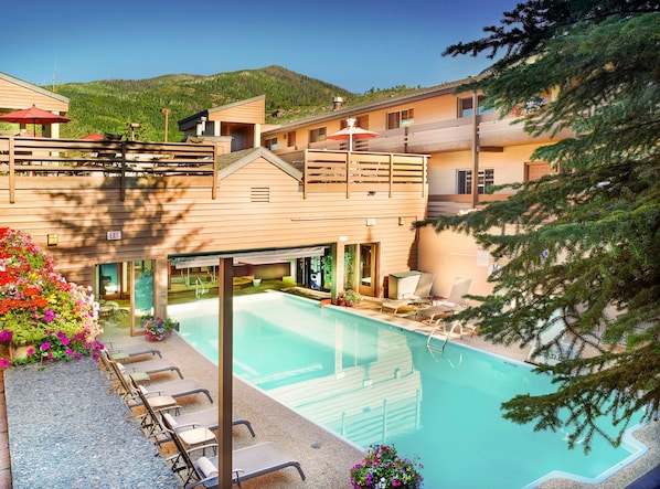 Enjoy the sunshine and vibrant flowerbeds surrounding the shared pool and hot tub area, perfect for relaxation in a cozy alpine condo setting.