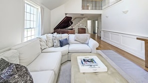 Vaulted living room with comfortable seating, large flat screen TV and grand piano