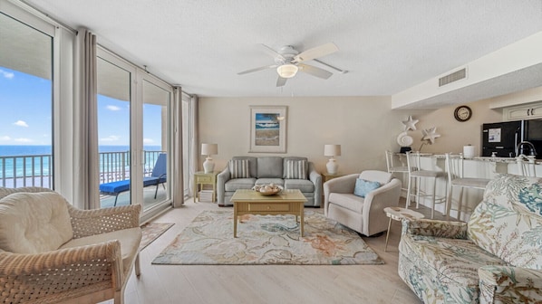 This inviting living room offers a coastal retreat with a breathtaking Gulf-front view. The soft neutral palette is accented by ocean-inspired decor, including shell and starfish wall art. Floor-to-ceiling glass doors flood the space with natural light, l