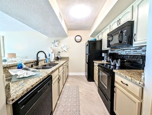 Welcome to your beachside kitchen retreat! This fully equipped space combines style and functionality with granite countertops, sleek black appliances, and creamy raised-panel cabinetry. The modern glass tile backsplash adds a coastal flair, while the spa