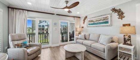 This bright and inviting living room features coastal-inspired decor, plush seating, and natural light streaming through sliding glass doors. With tasteful touches like turtle-themed accents and wood-look floors, it's a relaxing space perfect for unw