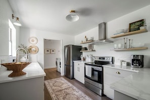The modern kitchen features a sleek stainless steel side-by-side refrigerator with a bottom freezer, an electric flat top range, floating shelves, and generous countertop space for effortless meal prep.