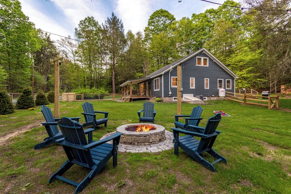 View of the house and nearby fire pit, surrounded by trees and string lights—perfect for cozy evenings with friends and family.