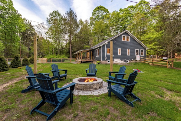 View of the house and nearby fire pit, surrounded by trees and string lights—perfect for cozy evenings with friends and family.