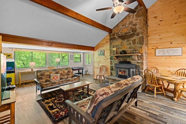 Gather around the crackling wood stove in this cozy living space, where tall ceilings, warm wood walls, and woodland decor invite you to truly unwind.