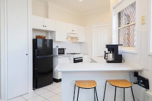 The compact kitchen makes mealtime easy, featuring a gas stove, oven, coffee machine, and microwave, along with a breakfast bar and stools for relaxed, casual dining.