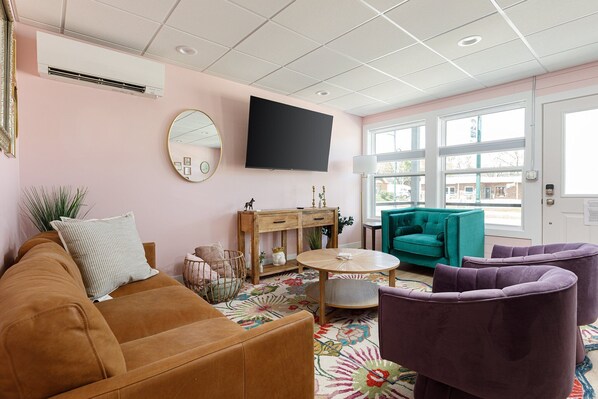 Enjoy the eclectic charm of this living space, complete with a colorful rug, stylish seating options, and a wall-mounted TV for your entertainment.