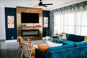 Snuggle up by the sleek electric fireplace, sink into plush velvet sofas, and soak in the natural light dancing off bold, vibrant décor. Whether you're binge-watching on the big screen or sipping wine under soft-glow lighting, this living room is the perfect vibe for your getaway. 