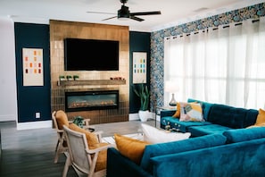 Snuggle up by the sleek electric fireplace, sink into plush velvet sofas, and soak in the natural light dancing off bold, vibrant décor. Whether you're binge-watching on the big screen or sipping wine under soft-glow lighting, this living room is the perfect vibe for your getaway.