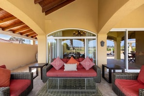 Spacious patio with comfortable wicker seating, bright red cushions, and a glass coffee table. Ideal for relaxing and enjoying the outdoor view, with a peaceful atmosphere under a high, arched ceiling.